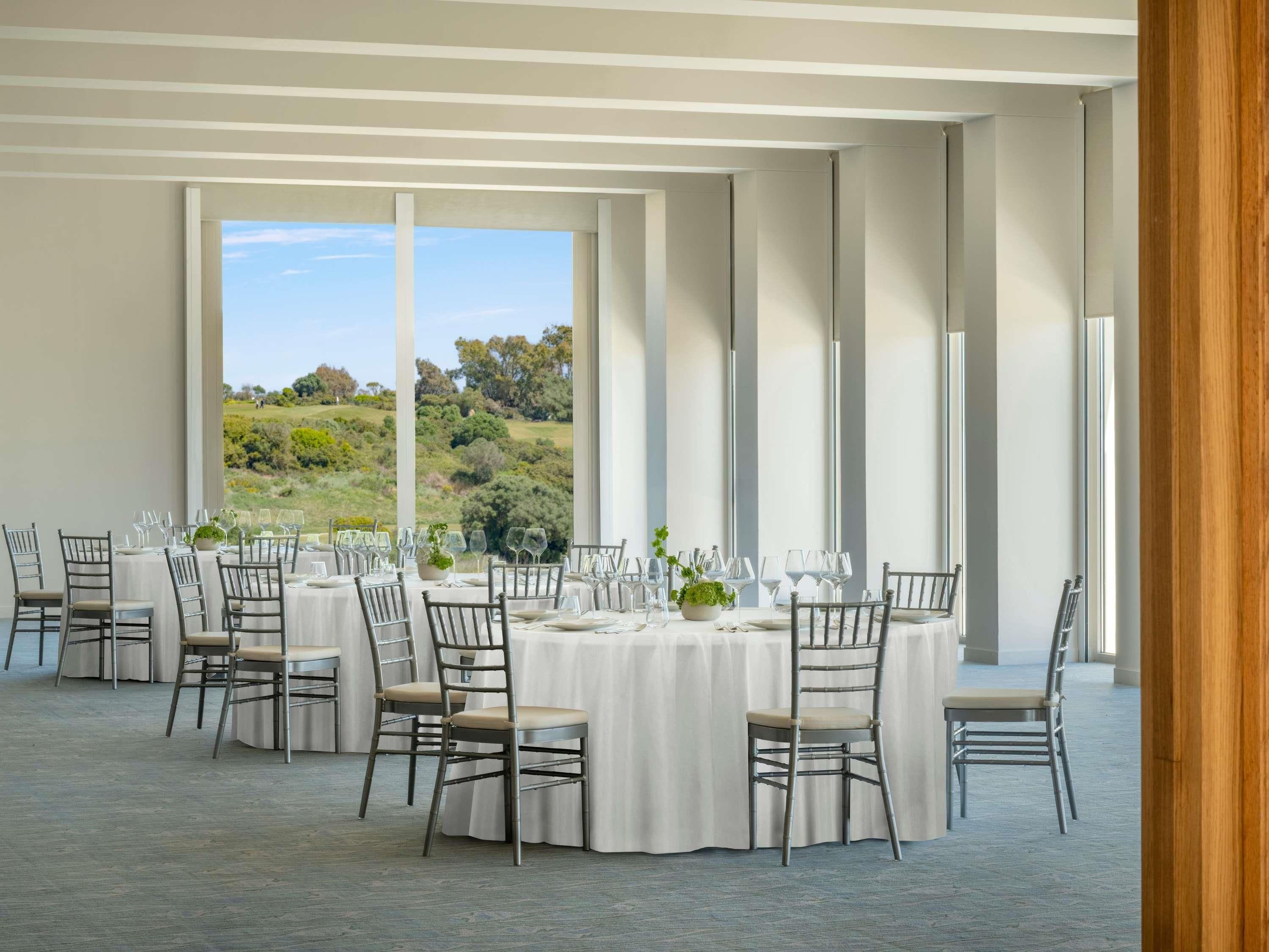 Un comedor con mesas y sillas redondas, amplias ventanas con vistas al paisaje y una decoración de diseño moderno.