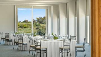 Un comedor con mesas y sillas redondas, amplias ventanas con vistas al paisaje y una decoración de diseño moderno.
