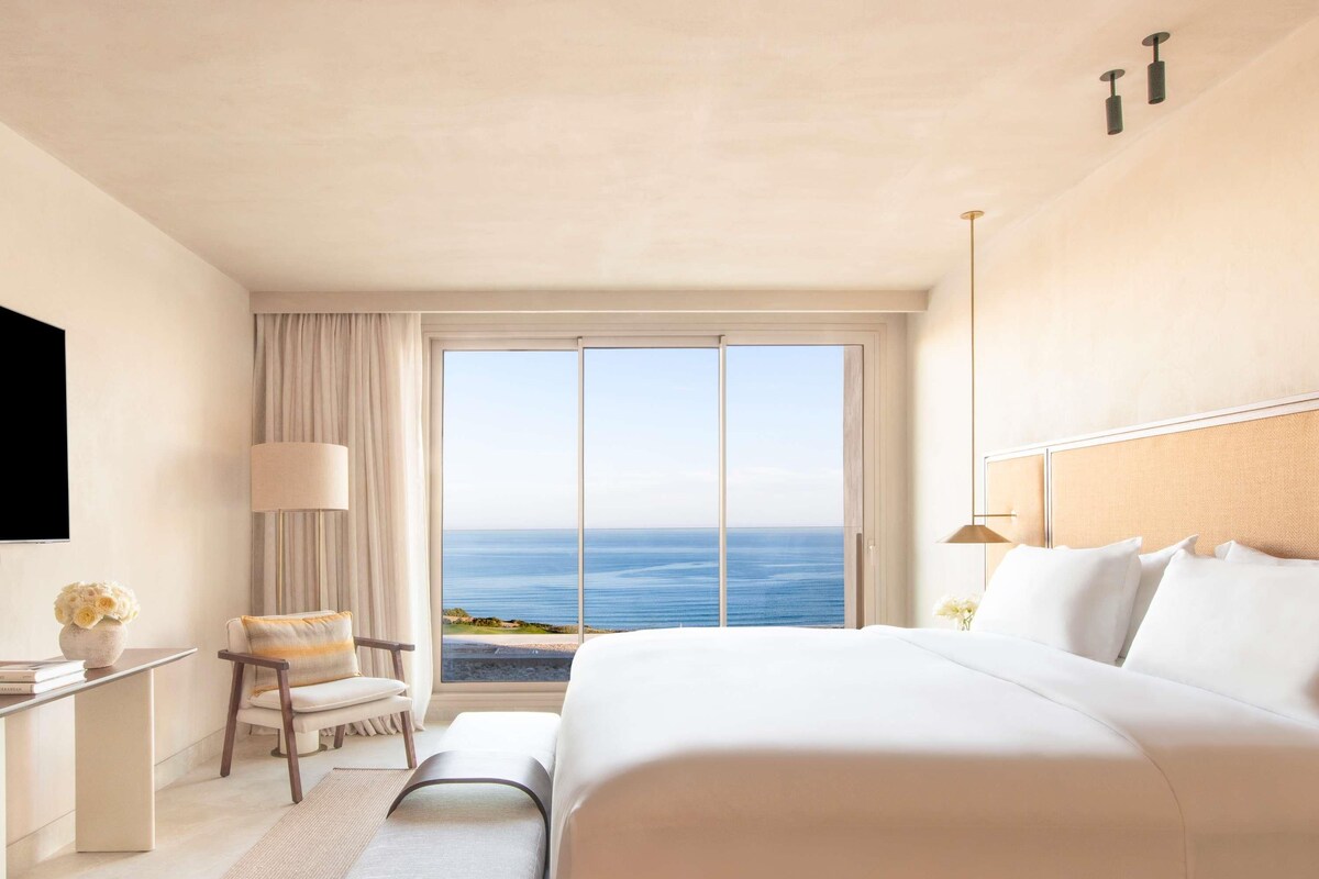 Une chambre d’hôtel avec un grand lit, une chaise, un bureau, une télévision et une vue sur l’océan.