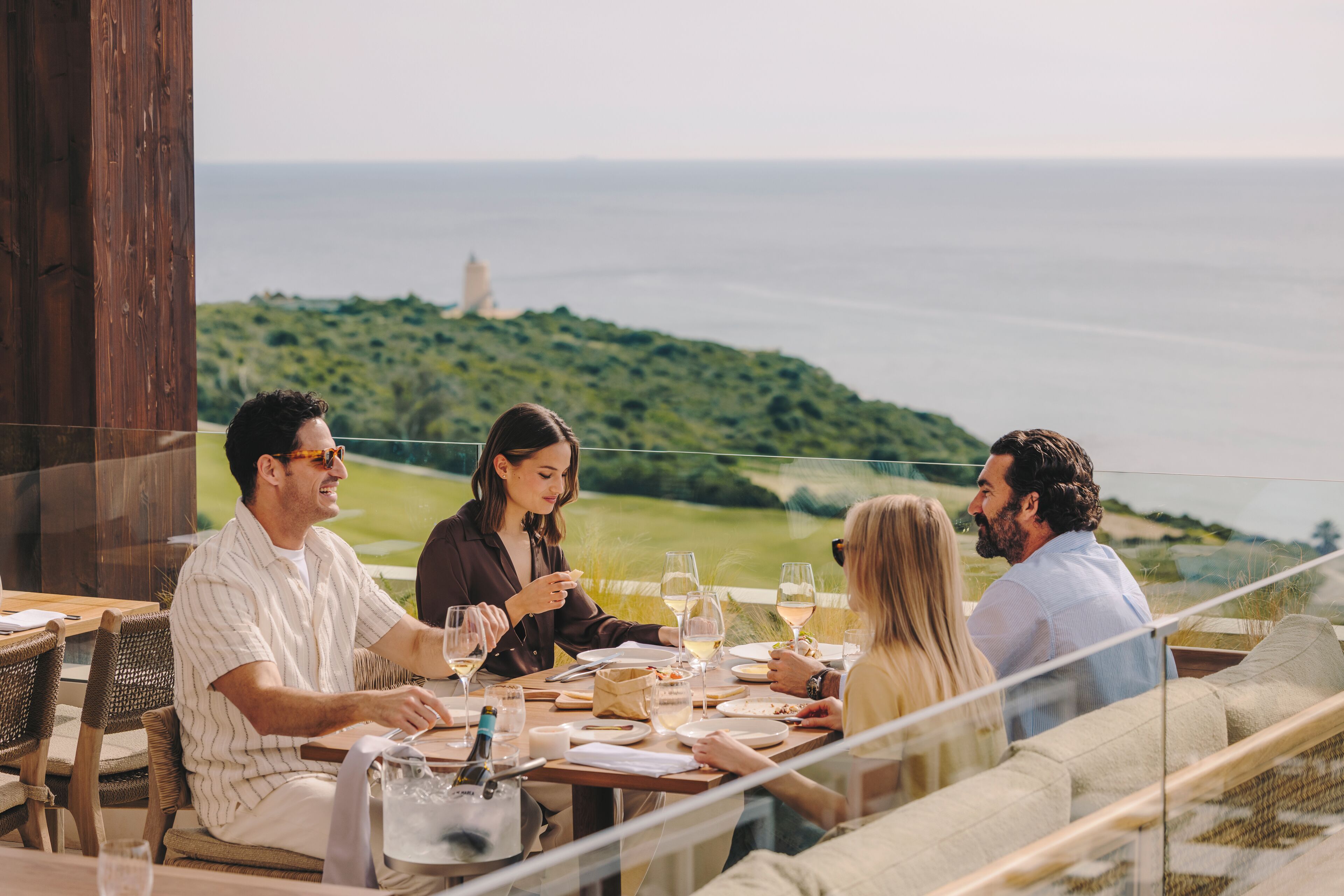 Un grupo de personas cenando en una mesa con vistas panorámicas al océano.
