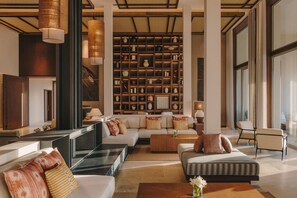 Ein geräumiger Wohnbereich mit einer großen Couch, einem Couchtisch und einem Bücherregal voller dekorativer Gegenstände.