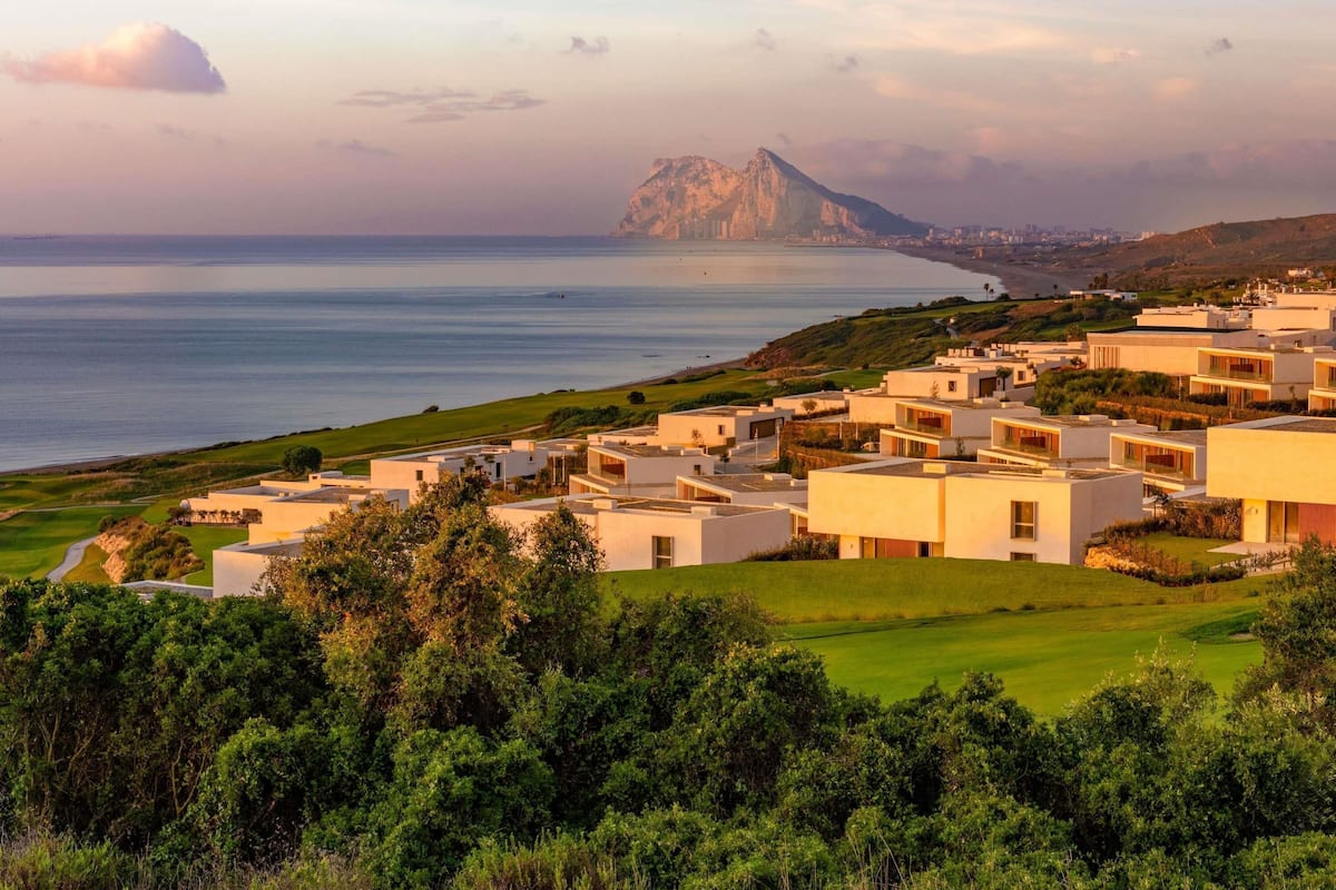 A coastal residential area with modern buildings, a golf course, and a prominent mountain in the background.