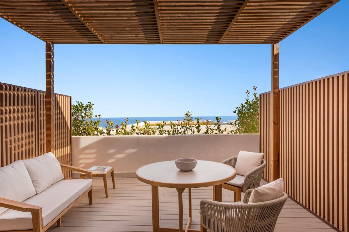 Une terrasse en bois avec une table ronde et deux chaises, donnant sur une plage.