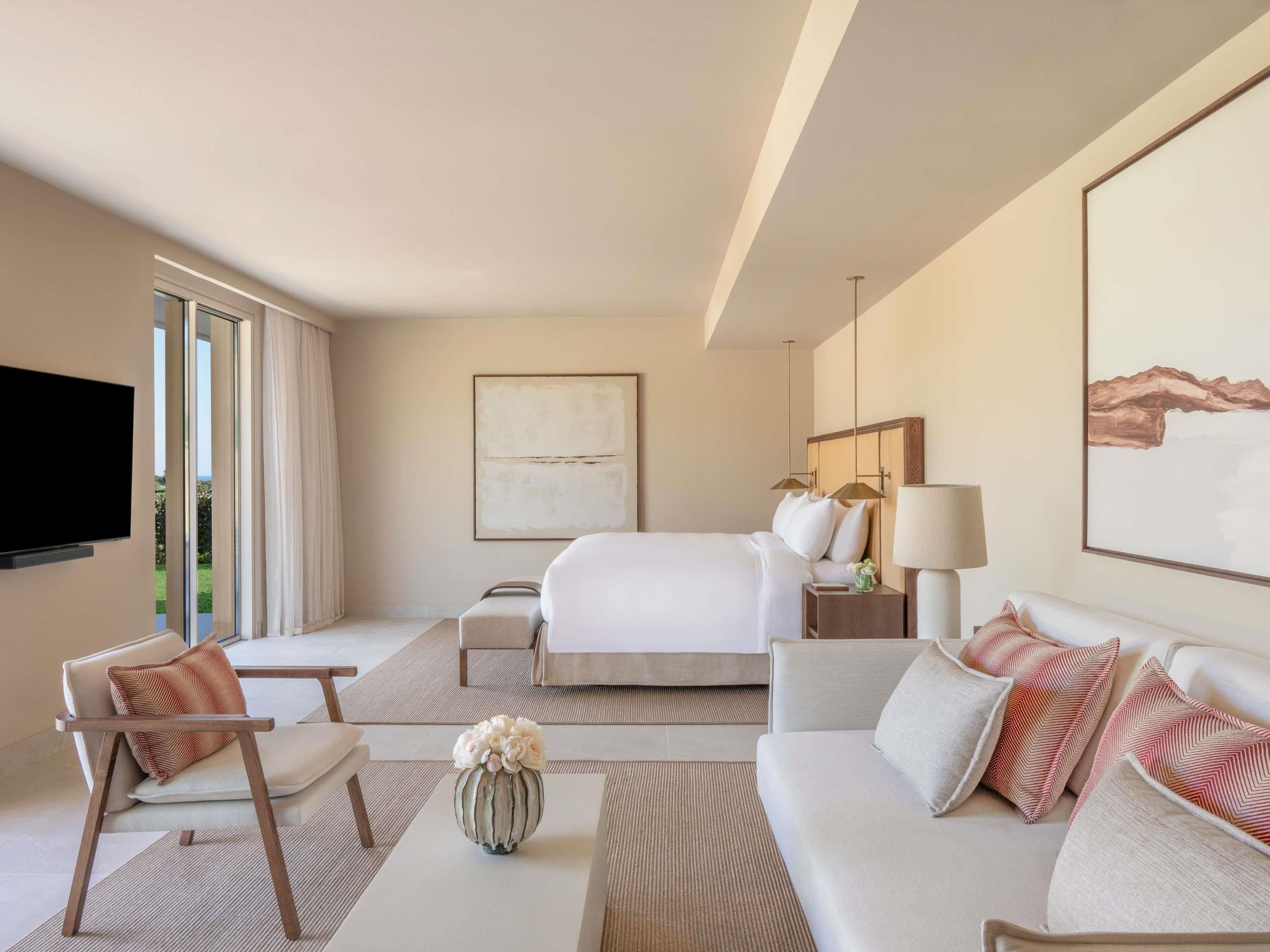 A hotel room with a bed, a sofa, a TV, a lamp, and a painting on the wall.