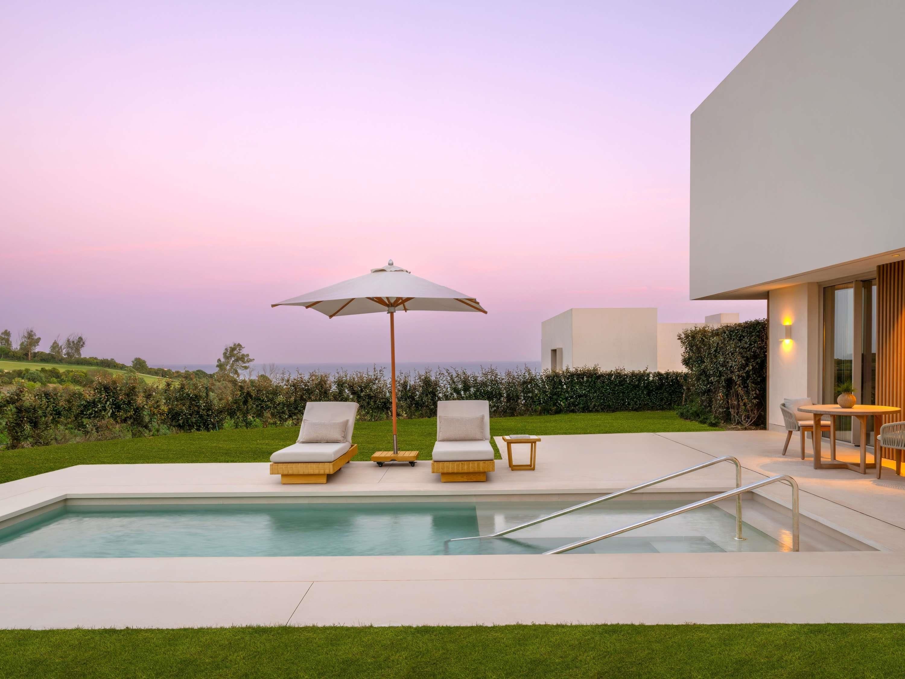 Zona de piscina exterior moderna amb gandules, una taula i un parasol.