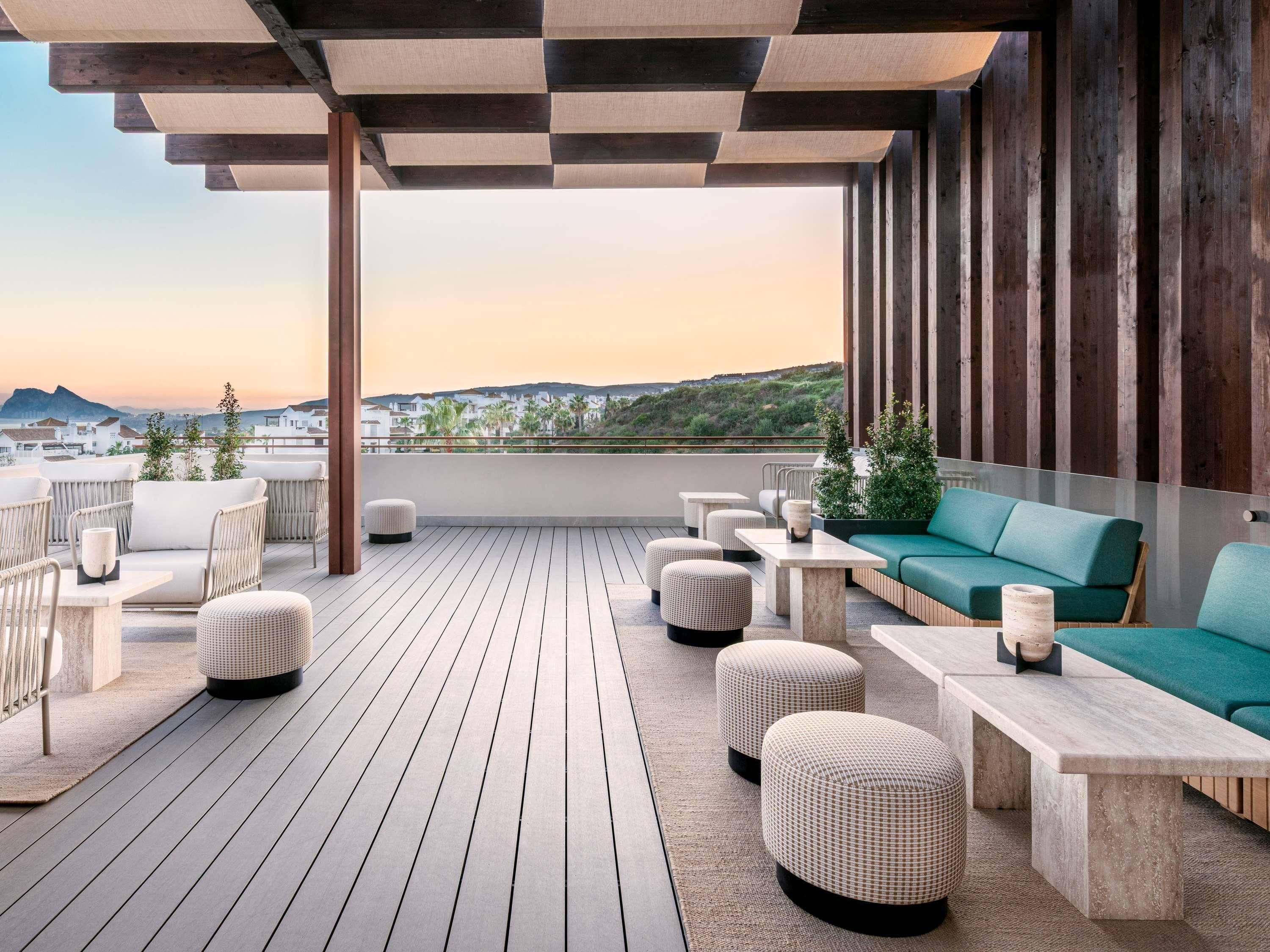 Una terraza de madera con mobiliario exterior, un sofá verde y vista a un paisaje costero.
