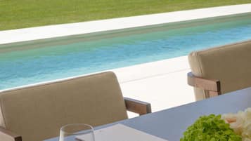 Una mesa con un vaso de agua, un bloc de notas y un bolígrafo, con vista a una piscina.