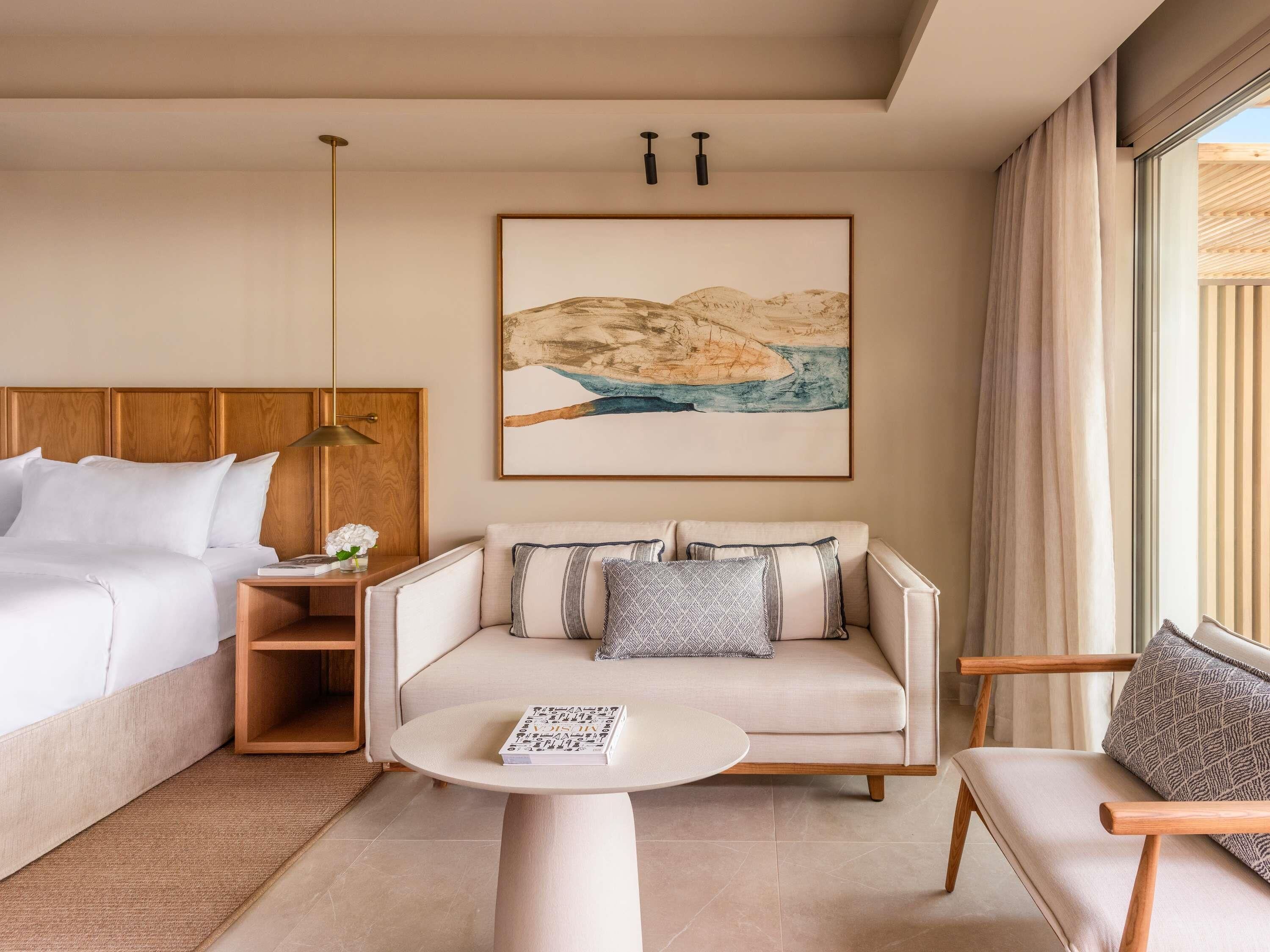 A hotel room with a bed, a sofa, a coffee table, and a painting on the wall.