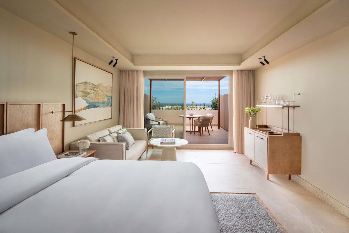 Une chambre d’hôtel moderne dotée d’un grand lit, d’un canapé, d’une table à manger et offrant une vue sur l’océan.