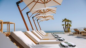 Eine Reihe von Liegestühlen mit Sonnenschirmen, ein Poolbereich und Blick auf das Meer.
