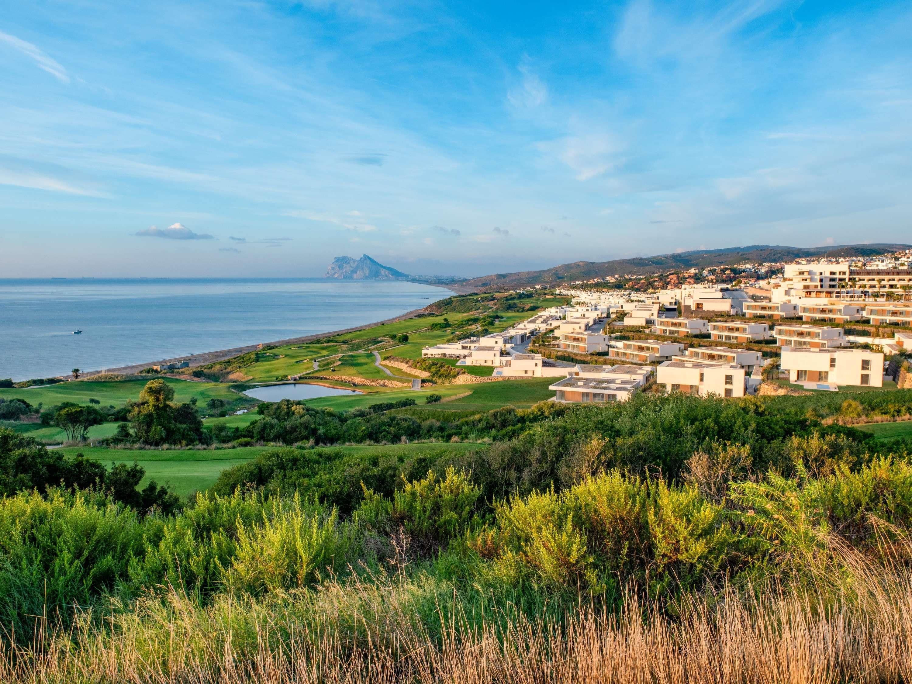 Un quartier résidentiel situé sur la côte, avec des immeubles modernes, un terrain de golf et une vue sur la mer.