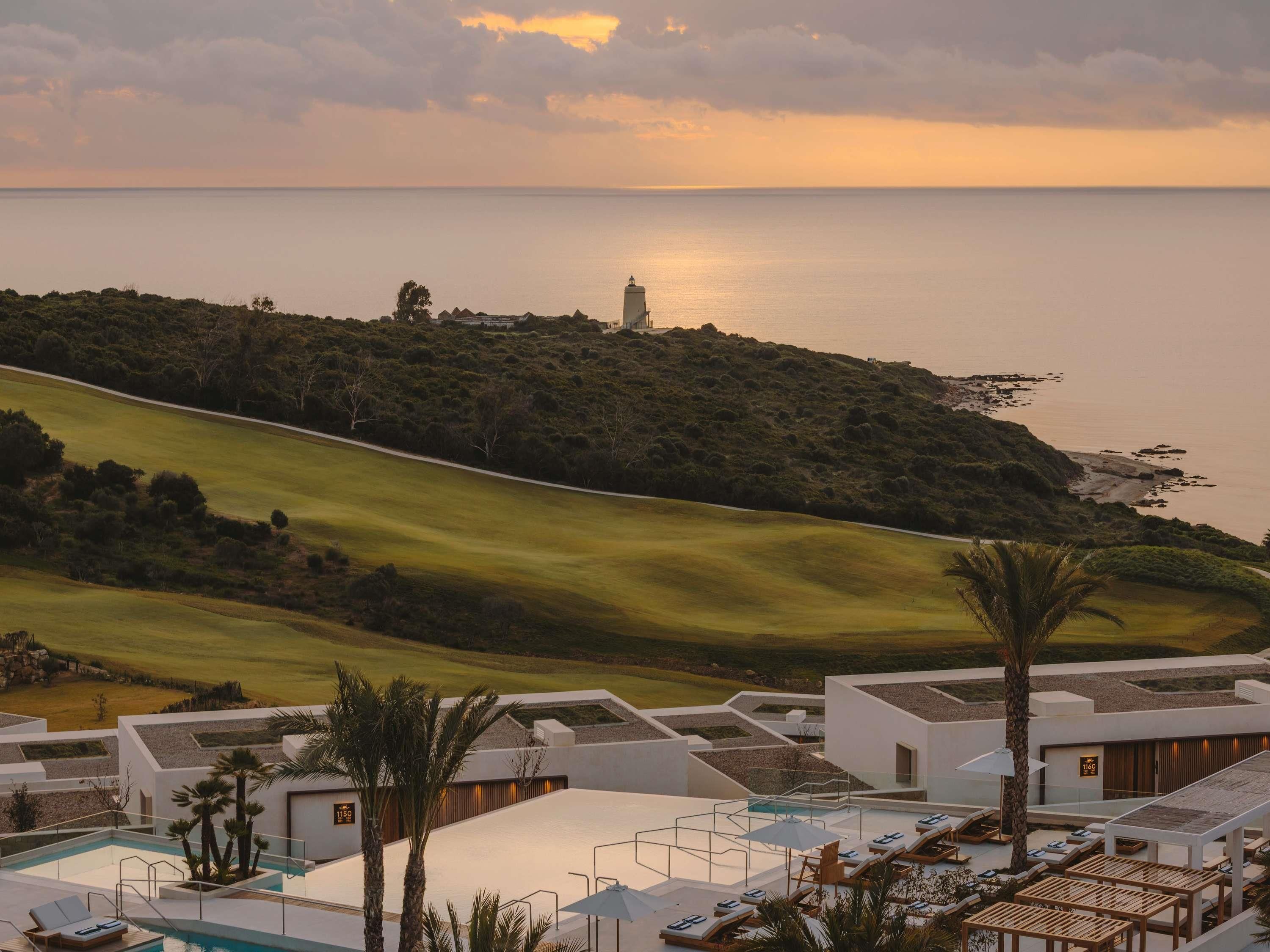 A resort with a swimming pool, lounge chairs, and a view of the sea.