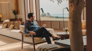 Un hombre sentado en un sofá en una habitación luminosa con vistas al exterior.
