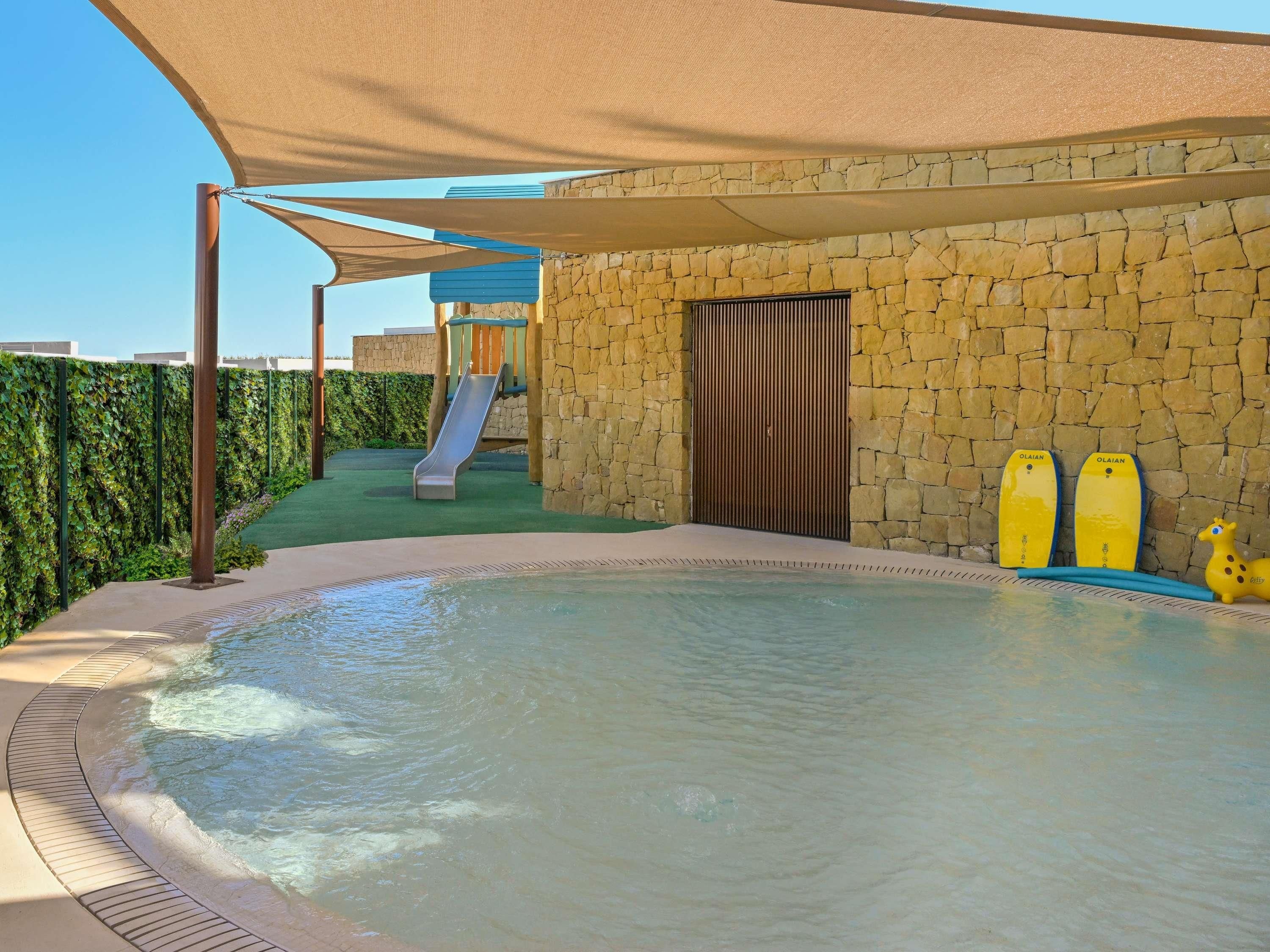 A pool area with a slide, a covered seating area, and a stone wall.