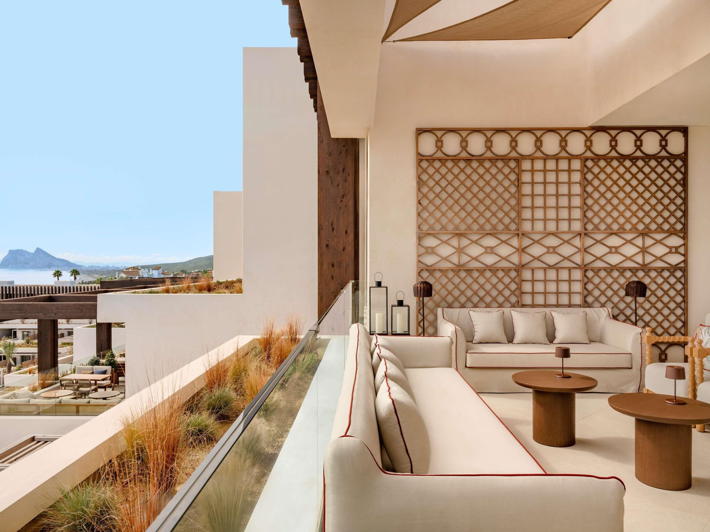 Un área de estar moderna al aire libre con un sofá y dos mesas redondas, con vistas a un paisaje costero.