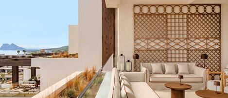 Un área de estar moderna al aire libre con un sofá y dos mesas redondas, con vistas a un paisaje costero.