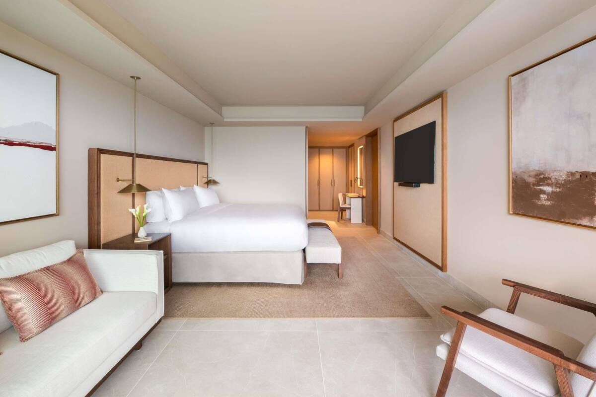 A modern hotel room with a large bed, a sofa, a chair, a desk, and a TV.