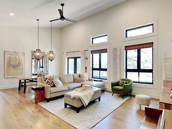 Relax in this stylish living room with a high ceiling, sectional sofa, and armchair, offering views of the outdoors.