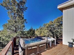 Relax in a serene outdoor space with a hot tub surrounded by lush greenery and tall trees.