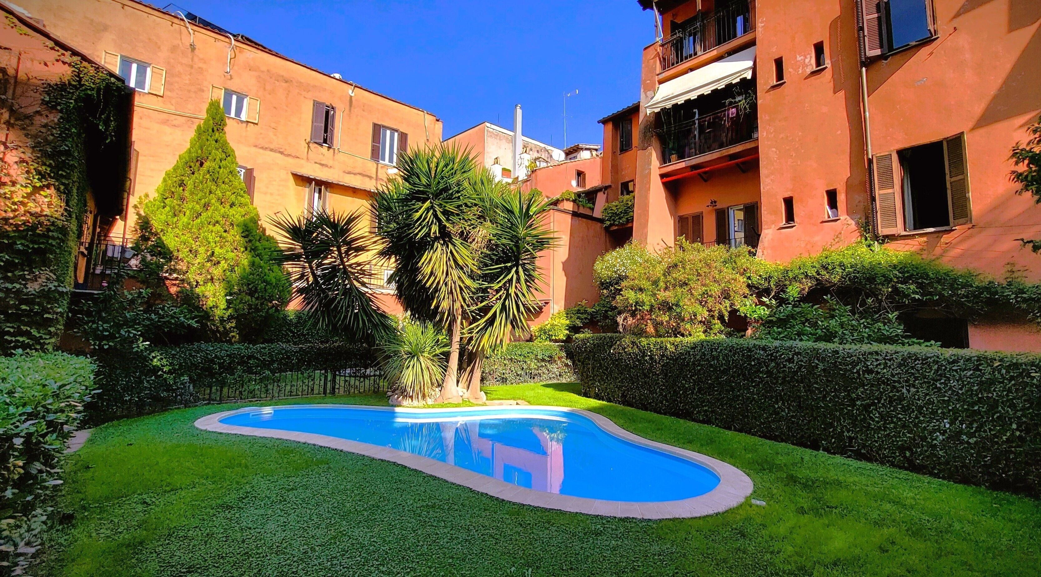 A courtyard with a swimming pool, surrounded by well-maintained hedges and trees.