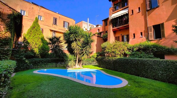 Un patio con piscina, rodeado de setos y árboles bien cuidados.