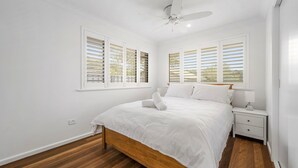 Une chambre à coucher avec un lit, des tables de chevet, un ventilateur de plafond et des fenêtres équipées de stores.