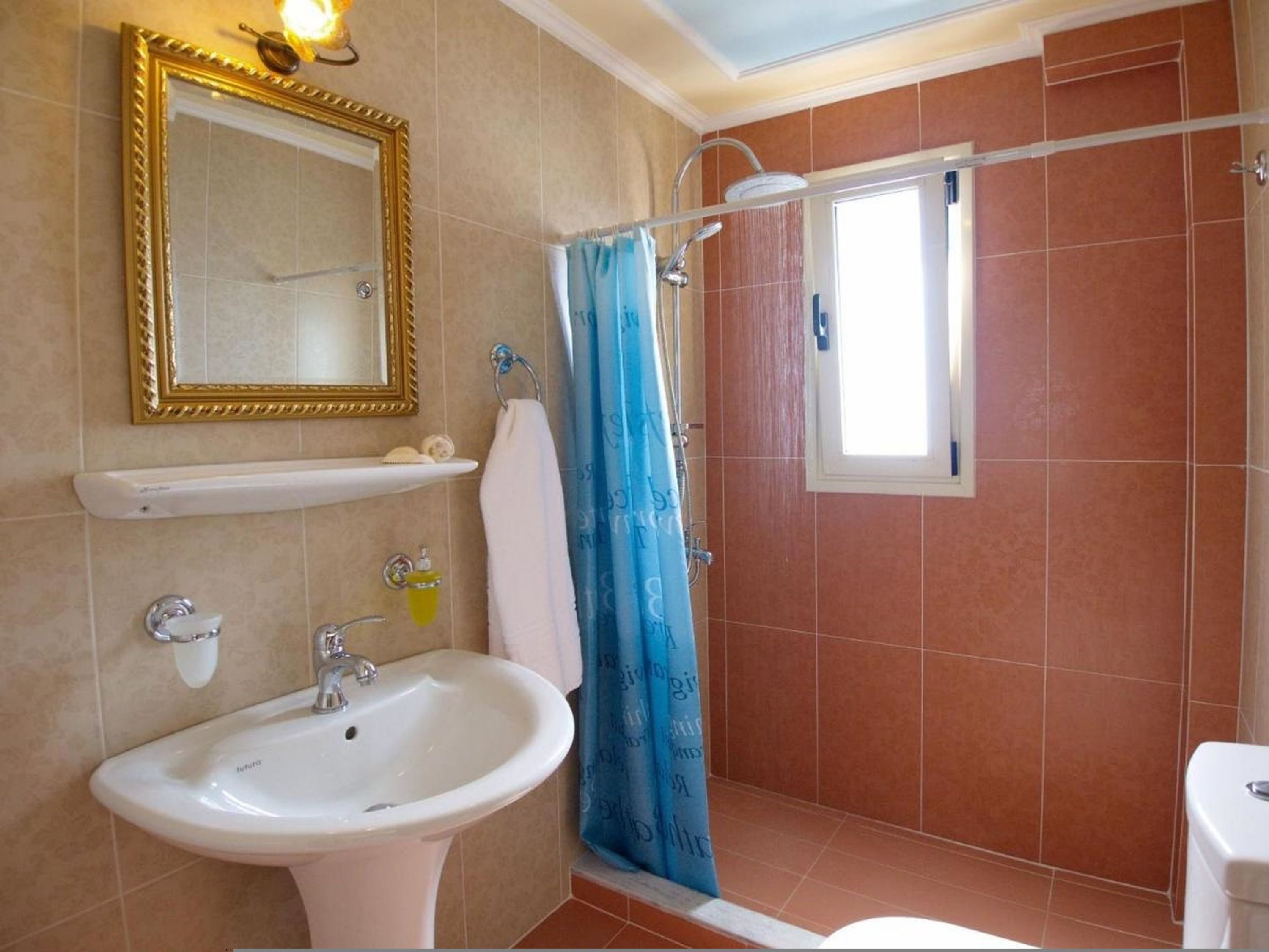 A bathroom with a sink, mirror, shower, and a window.