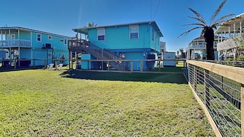 A blue building with a staircase leading to a balcony, surrounded by a fenced yard with grass.