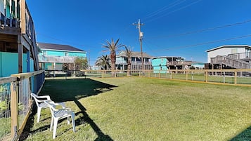 A grassy area with a wooden fence, a white plastic chair, and a building with a turquoise facade.