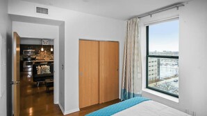 A modern hotel room with a large bed, a wardrobe, a view of the city, and a kitchenette in the background. - Stylish Top Floor Condo in Downtown Indianapolis, Mile Square Neighborhood  (Indianapolis)