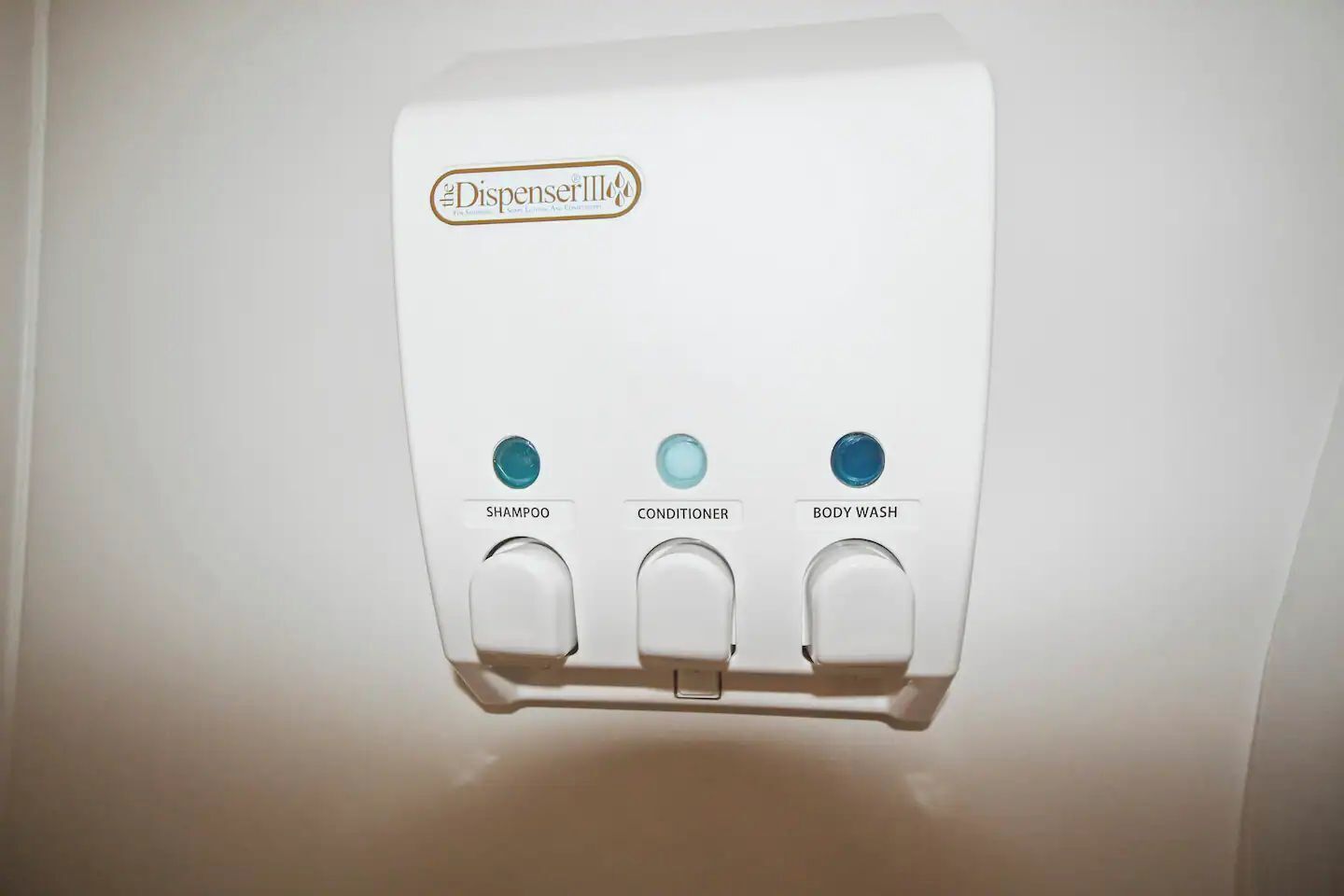 A wall-mounted dispenser with three buttons labeled "Shampoo," "Conditioner," and "Body Wash."