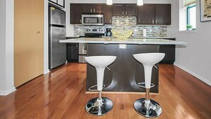 A modern kitchen with dark wooden cabinets, stainless steel appliances, and a central island with two white bar stools. - Stylish Top Floor Condo in Downtown Indianapolis, Mile Square Neighborhood  (Indianapolis)