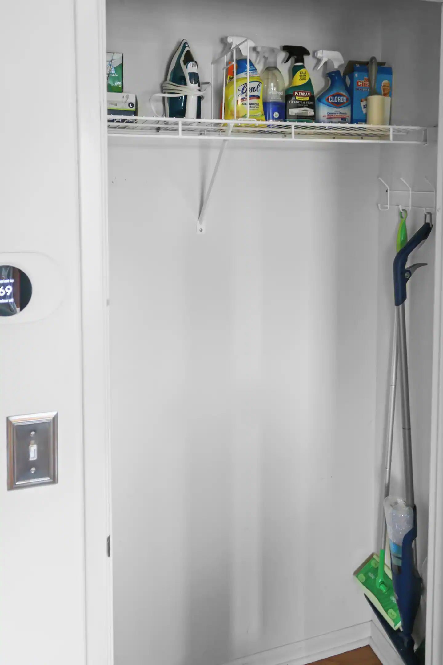 Een kast met planken vol schoonmaakspullen en een dweil.