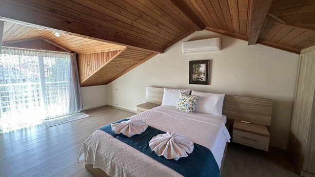 A bedroom with a sloped ceiling, a bed with a blue and white duvet, two bedside tables, and a framed picture on the wall.