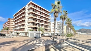 A multi-story hotel with balconies, a beachside location, and palm trees. - V023 - Roses Platja (Roses)
