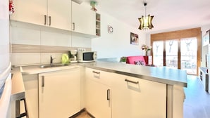 A modern kitchen with white cabinets, a stainless steel sink, and a built-in microwave. There is a wooden floor and a large window with a view of the outdoors. - V023 - Roses Platja (Roses)