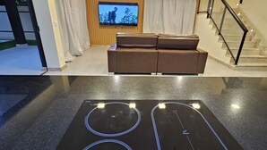 A modern living room with a brown leather sofa, a flat-screen TV mounted on a wooden wall, and a staircase with black railings. - Casa Luna (Camaçari)