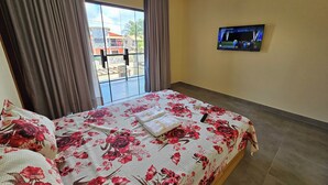 A hotel room with a bed, curtains, a TV, and a view of the outside. - Casa Luna (Camaçari)