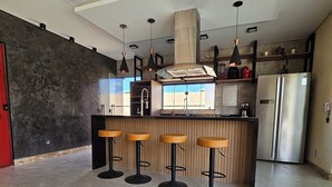 A modern kitchen with a central island, bar stools, pendant lighting, and stainless steel appliances. - Casa Luna (Camaçari)