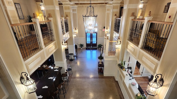 A grand hallway with ornate ceiling and chandeliers, leading to a reception area with a blue door and a view of a dining area with tables and chairs. - Historic Griffin Hotel (Griffin)