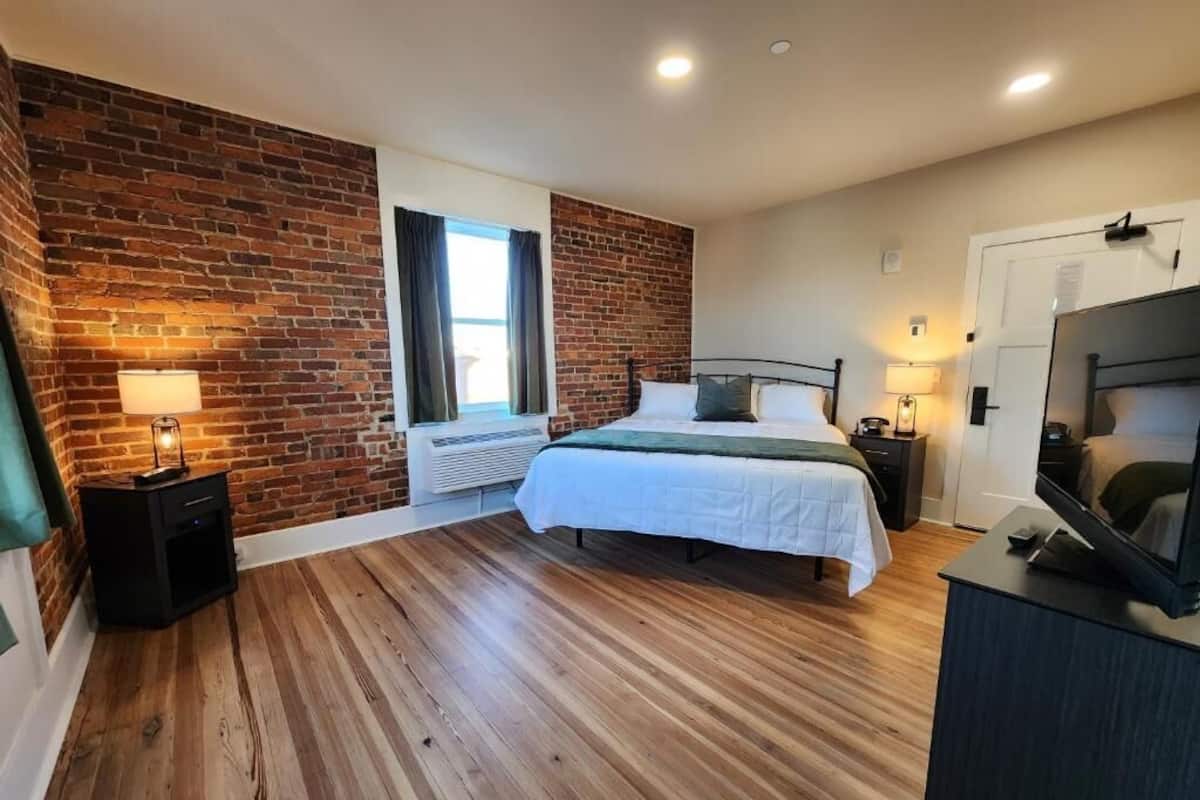 A bedroom with a brick wall, a bed, a TV, and a window.