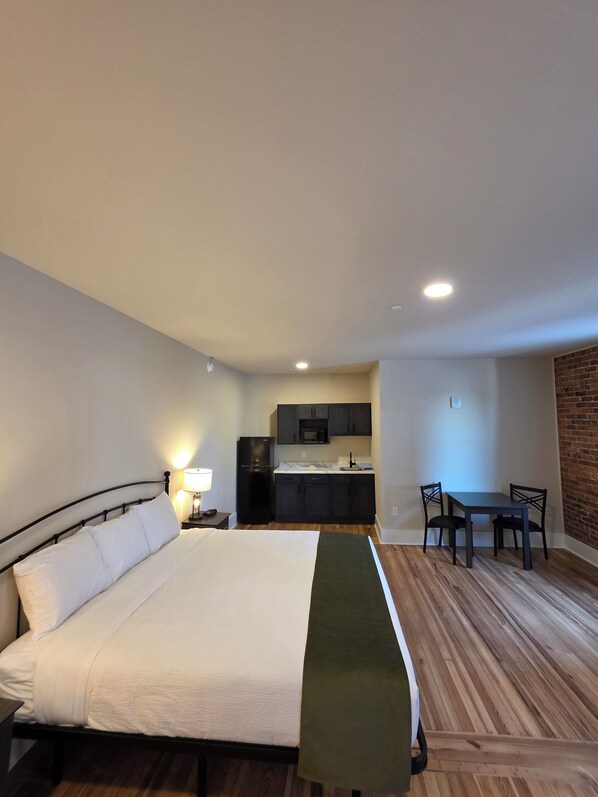 A bedroom with a bed, a bedside table with a lamp, a kitchenette with a refrigerator and microwave, and a dining area with a table and chairs. - Historic Griffin Hotel (Griffin)
