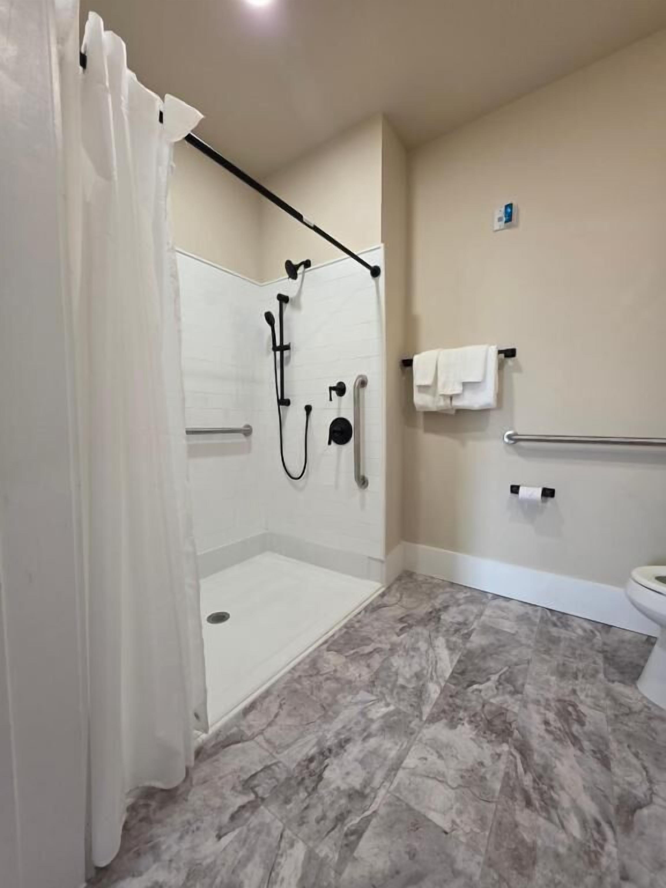 Un baño moderno con cabina de ducha, barras de apoyo, inodoro y toallero.