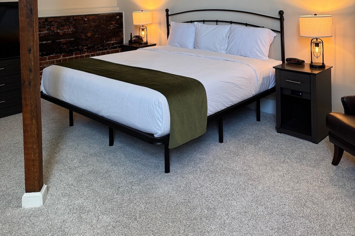 A bedroom with a bed, two bedside tables with lamps, a ceiling fan, and a brick wall.
