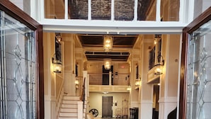 A grand entrance with a black doormat reading "HG" leading to a spacious foyer with a staircase, chandeliers, and a piano. - Historic Griffin Hotel (Griffin)