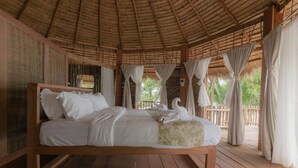 Una cama de madera con ropa de cama blanca, un techo de paja y cortinas.
