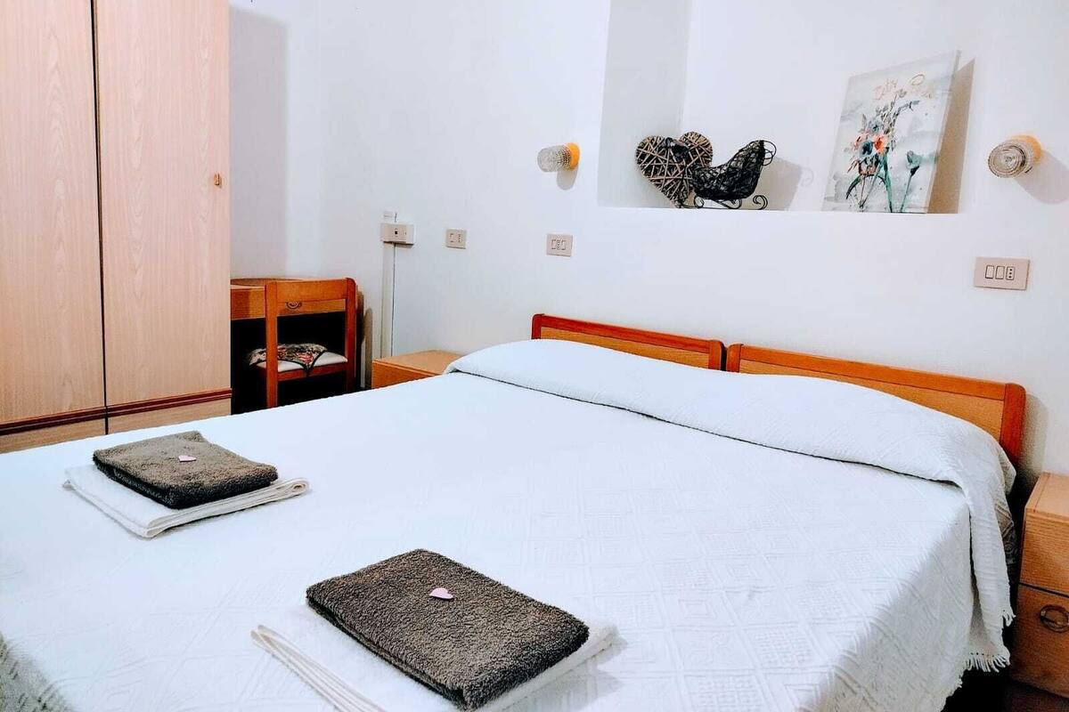 Um quarto com uma cama, um guarda-roupa de madeira, uma cadeira de madeira pequena e uma luminária fixada na parede.