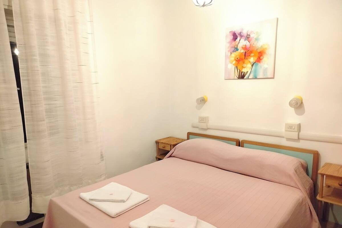 Um quarto com uma cama, duas mesas de cabeceira, uma luminária na parede e um quadro.