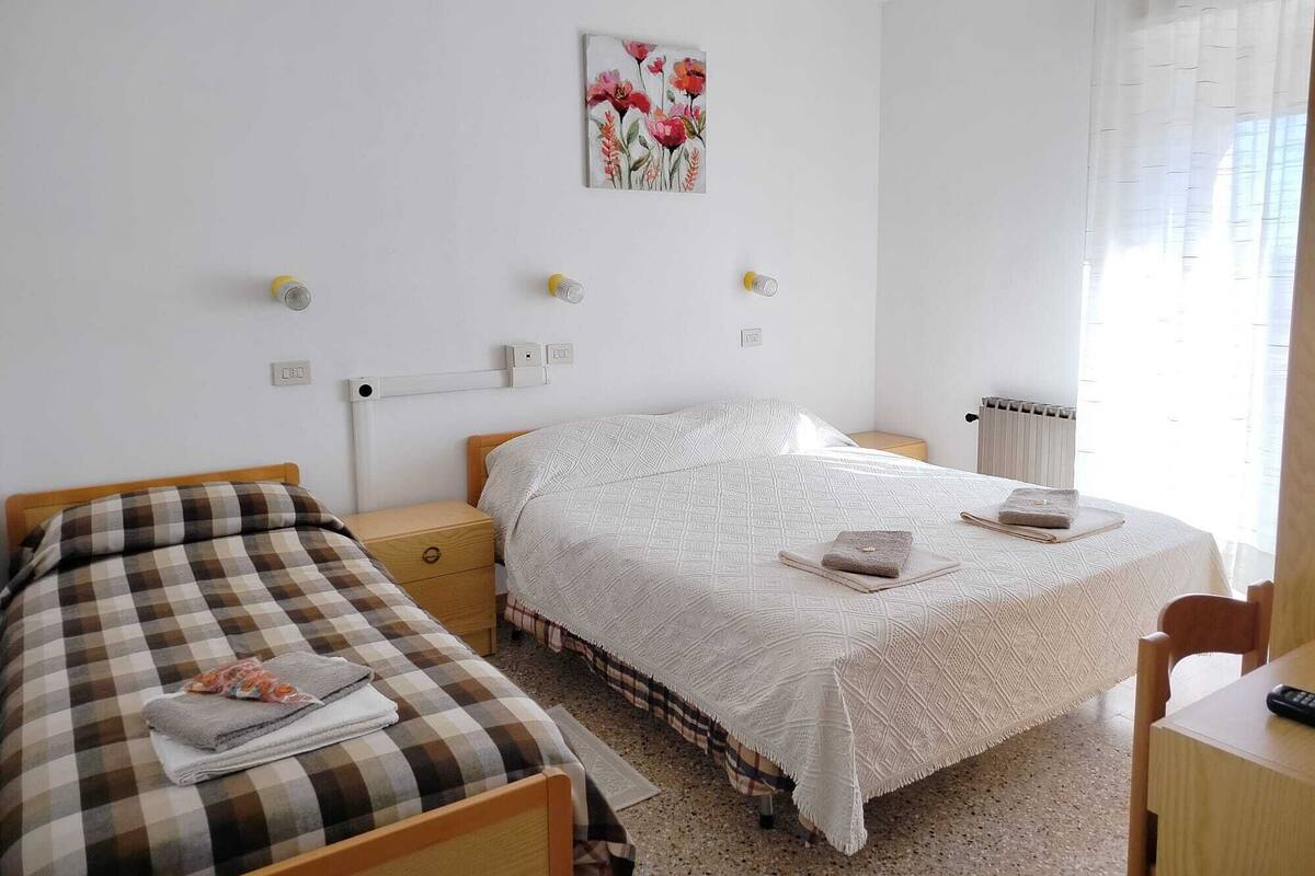 Quarto com duas camas, uma mesinha de cabeceira, um radiador e um quadro na parede.