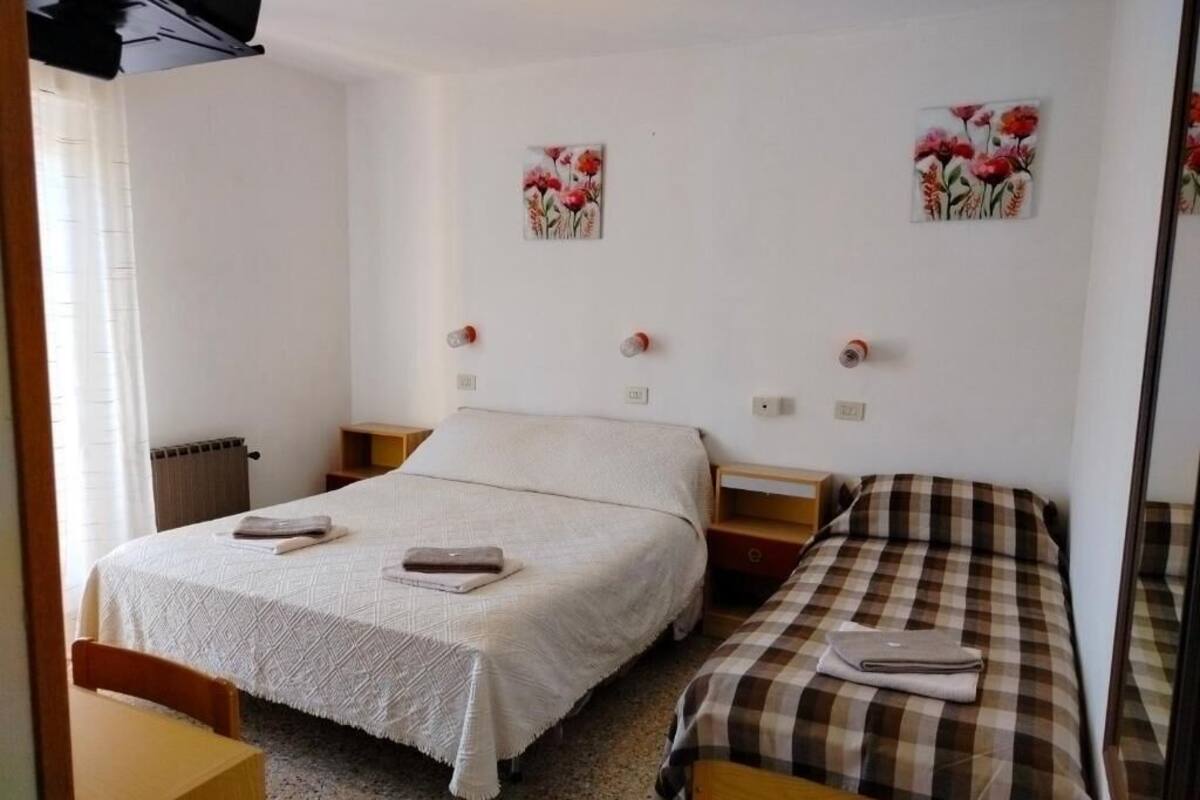 Quarto com duas camas, uma mesa de cabeceira de madeira, uma mesinha e um radiador.